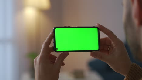 Mann-Hält-Smartphone-Horizontal-Und-Betrachtet-Nahaufnahme-Eines-Videos-Auf-Einem-Grünen-Bildschirm-Für-Virtuelle-Bilder-Mit-Chroma-Key-Technologie